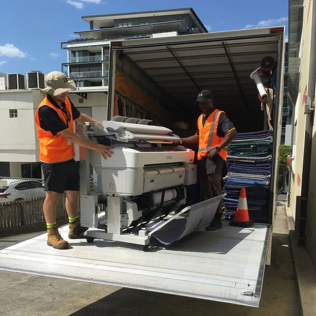 Two movers carefully handling office equipment on a truck tail lift