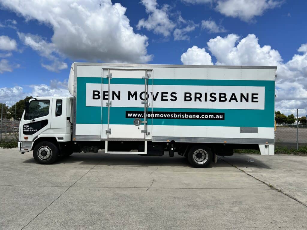 A medium moving truck parked on concrete with blue skies and clouds in the background